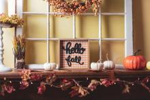 hello fall sign sitting on top of a table around fall decorations